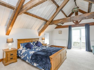 A bedroom with wooden bed and nightstands under exposed wooden beams at Caerdegog Ganol in Cemlyn near Cemaes Bay