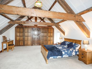 A bedroom with wooden bed frame and side tables under exposed wooden beams at Caerdegog Ganol in Cemlyn near Cemaes Bay