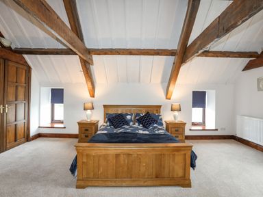A bedroom with a wooden bed and side tables with lamps under exposed ceiling beams at Caerdegog Ganol in Cemlyn near Cemaes Bay