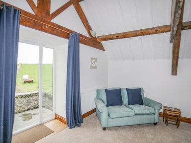 A sitting room with a two-seater sofa and blue curtains by a glass door at Caerdegog Ganol Cemlyn near Cemaes Bay