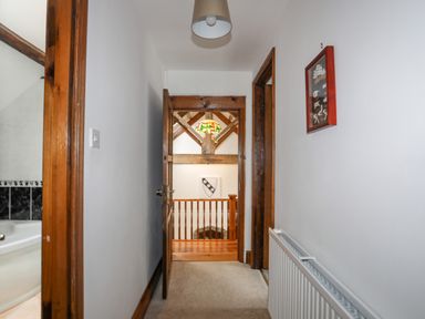 A hallway with doors leading to rooms and a view of a wooden railing and stained glass light at Caerdegog Ganol in Cemlyn near Cemaes Bay