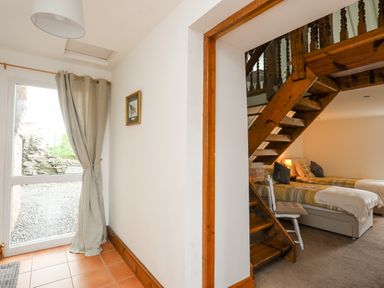 A hallway with a glass door and curtain next to a bedroom with two single beds under wooden stairs at Caerdegog Ganol in Cemlyn near Cemaes Bay