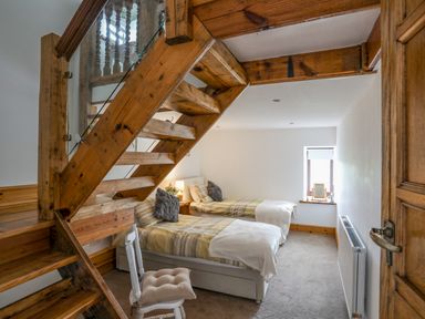 A bedroom with two single beds a wooden staircase and a chair at Caerdegog Ganol in Cemlyn near Cemaes Bay