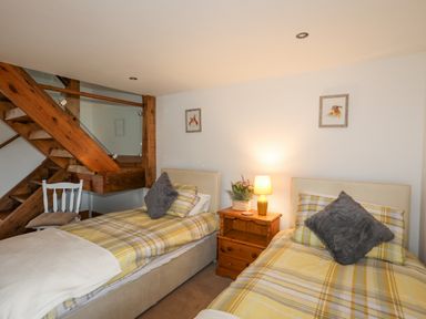 A bedroom with two single beds with yellow plaid bedding a wooden nightstand with a lamp and flowers and wooden stairs with a white chair at Caerdegog Ganol Cemlyn near Cemaes Bay