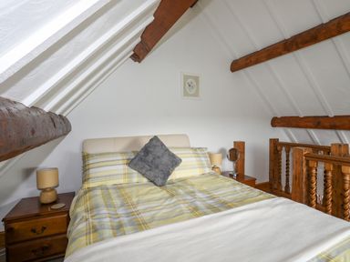 A bedroom with a bed with yellow plaid bedding and wooden bedside tables with lamps and wooden beams on the ceiling at Caerdegog Ganol in Cemlyn near Cemaes Bay