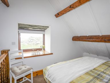 A bedroom with a bed a chair and a window with a flower and happy sign at Caerdegog Ganol in Cemlyn near Cemaes Bay