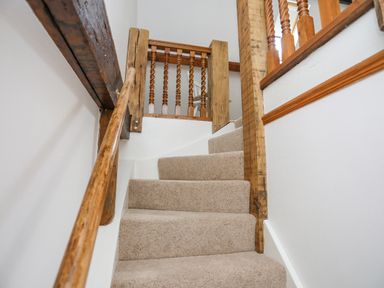 A carpeted staircase with wooden handrails and balusters at Caerdegog Ganol in Cemlyn near Cemaes Bay