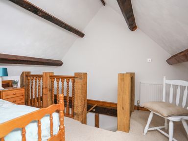 An attic bedroom with wooden bed frame wooden nightstand with lamp wooden stair railing and white chair with cushion at Caerdegog Ganol Cemlyn near Cemaes Bay
