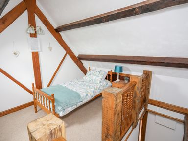 A small bedroom with a single bed a bedside table with a lamp and wooden beams at Caerdegog Ganol in Cemlyn near Cemaes Bay