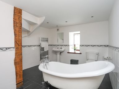 A bathroom with a freestanding bathtub toilet pedestal sink towel rack and wooden beam at Caerdegog Ganol Cemlyn near Cemaes Bay