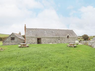 A grassy yard with two wooden picnic tables in front of a stone building at Caerdegog Ganol in Cemlyn near Cemaes Bay
