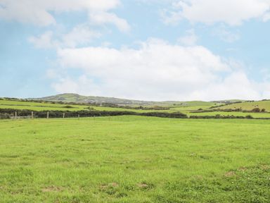 Green pasture land with fence and rolling hills under a blue sky with clouds at Caerdegog Ganol in Cemlyn near Cemaes Bay