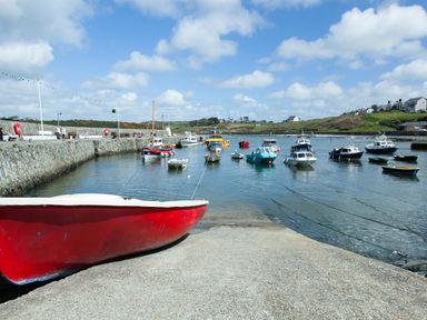 A harbor with multiple small boats moored near a stone pier and a red boat on a concrete ramp at Caerdegog Ganol in Cemlyn near Cemaes Bay
