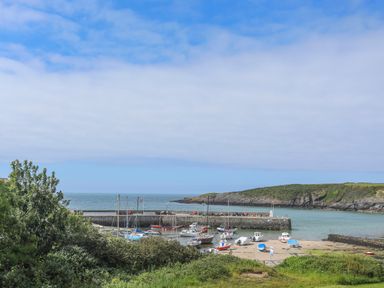 A harbor with boats docked near a stone pier and grassy hills at Caerdegog Ganol in Cemlyn near Cemaes Bay