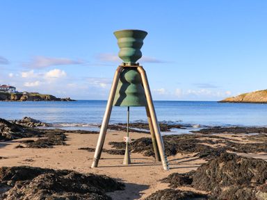 A metal beacon structure on a sandy beach with seaweed and the ocean in the background at Caerdegog Ganol in Cemlyn near Cemaes Bay