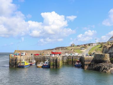 A small harbor with several boats docked and vehicles parked on the pier at Caerdegog Ganol in Cemlyn near Cemaes Bay