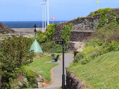 A coastal path with a black signpost and a bench near a stone wall at Caerdegog Ganol in Cemlyn near Cemaes Bay