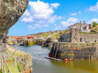 A small harbor with boats docked near stone buildings and a rocky cliffside at Caerdegog Ganol in Cemlyn near Cemaes Bay