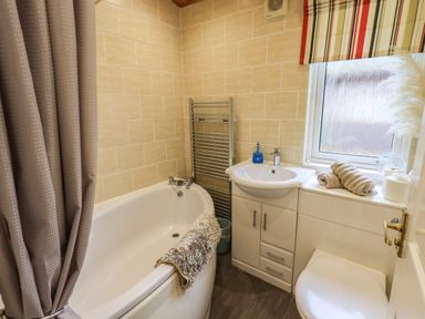 A bathroom with a bathtub a sink toilet and a window with towels on the windowsill at Our Happy Place Lakeside 16 Borwick near Carnforth