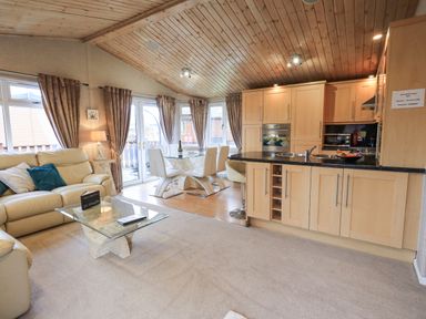An open living room and kitchen with beige sofas glass dining table and wooden ceiling at Our Happy Place Lakeside 16 Borwick near Carnforth