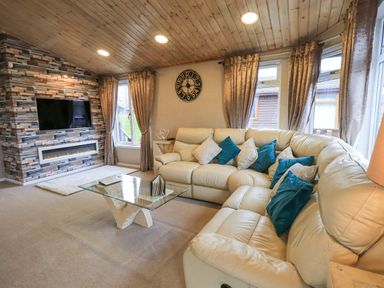 A living room with a cream leather sofa and blue cushions a glass coffee table a wall-mounted TV and a fireplace at Our Happy Place in Lakeside 16 Borwick near Carnforth