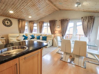 A living area with a beige sectional sofa and a glass dining table with white chairs at Our Happy Place Lakeside 16 Borwick near Carnforth