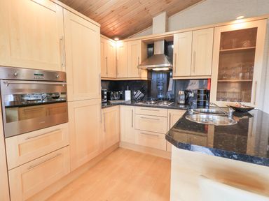 A kitchen with wooden cabinets black countertops a stove oven and a double sink at Our Happy Place Lakeside 16 Borwick near Carnforth