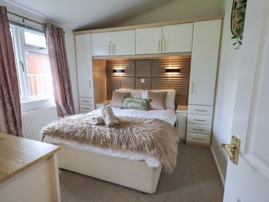 A bedroom with a double bed built in cupboards and a window at Our Happy Place Lakeside 16 Borwick near Carnforth