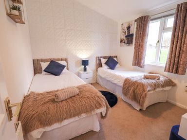 A bedroom with two single beds a nightstand lamp and a window at Our Happy Place Lakeside 16 Borwick near Carnforth