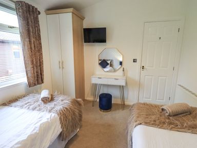 A bedroom with two beds a wardrobe a dressing table and a wall mounted tv at Our Happy Place Lakeside 16 Borwick near Carnforth