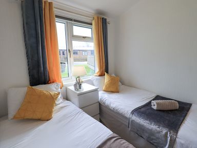 A bedroom with two single beds a bedside table between the beds and a window with curtains at Our Happy Place Lakeside 16 Borwick near Carnforth
