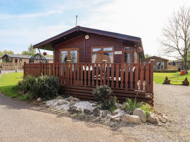 A wooden cabin with a fenced porch and plants in front at Our Happy Place Lakeside 16 Borwick near Carnforth