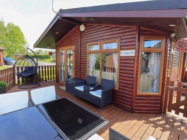 A wooden deck with outdoor furniture and hanging chair at Our Happy Place Lakeside 16 Borwick near Carnforth