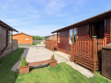 Wooden lodges with porches and small garden bench on grass at Our Happy Place Lakeside 16 Borwick near Carnforth