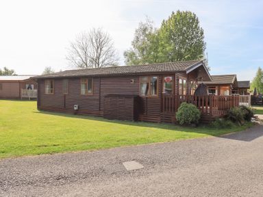 A brown wooden cabin with a covered porch and green lawn at Our Happy Place Lakeside 16 Borwick near Carnforth