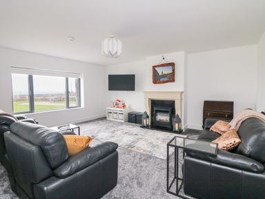 A living room with black leather sofas a fireplace and a wall-mounted television at Old Field House Slade near Fethard-On-Sea County Wexford