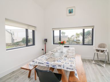 A dining room with a table set for eight people a vase with flowers on the table a high chair in the corner and large windows at Old Field House Slade near Fethard-On-Sea County Wexford
