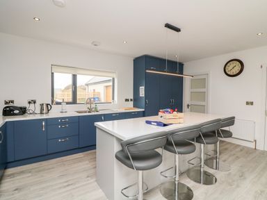A kitchen with blue cabinets an island with stools and a clock on the wall at Old Field House in Slade near Fethard-On-Sea County Wexford