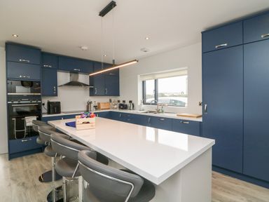 A kitchen with blue cabinets white countertop island and bar stools at Old Field House Slade near Fethard-On-Sea County Wexford