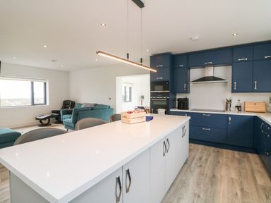 A kitchen with blue cabinets a white island and a living area with chairs and a window at Old Field House Slade near Fethard-On-Sea County Wexford