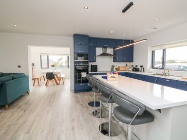 A kitchen with blue cabinets and gray bar stools next to a dining area with wooden benches at Old Field House Slade near Fethard-On-Sea County Wexford