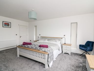 A bedroom with a bed with gray and white bedding two purple towels on the bed two nightstands with lamps a blue chair a framed picture on the wall at Old Field House Slade near Fethard-On-Sea County Wexford