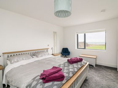 A bedroom with a double bed two purple towels a blue chair near a window and a storage bench at Old Field House Slade near Fethard-On-Sea County Wexford
