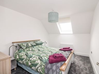 A bedroom with a bed covered in green leaf patterned bedding and two folded purple towels on top at Old Field House in Slade near Fethard-On-Sea County Wexford