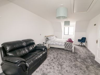 A bedroom with a black leather sofa a white bed with blankets and pillows a blue chair and a window at Old Field House Slade near Fethard-On-Sea County Wexford