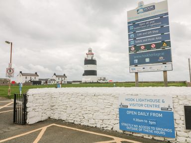 A lighthouse with visitor center signs and white buildings surrounding it at Hook Lighthouse