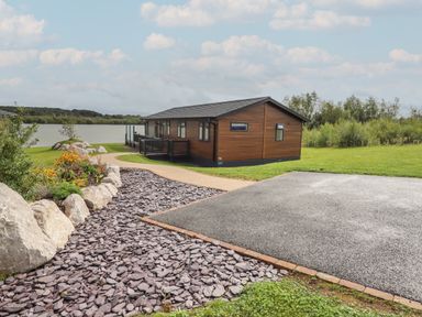 A wooden house with a tiled roof near a lake with a paved driveway and garden at 40 Delamere Point in Delamere