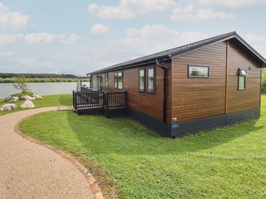 A brown wooden cabin with black trim on a grassy area near a lake at 40 Delamere Point in Delamere