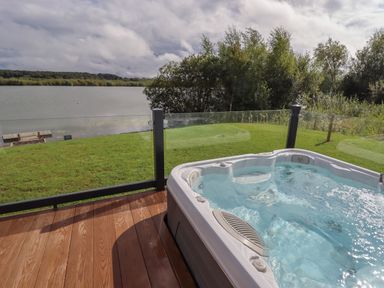 An outdoor hot tub on a wooden deck overlooking a grassy area with a lake and trees at 40 Delamere Point in Delamere