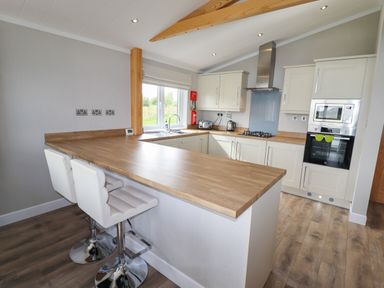 A kitchen with a wooden countertop, two white bar stools, white cabinets, gas stove, built-in oven and microwave at 40 Delamere Point in Delamere